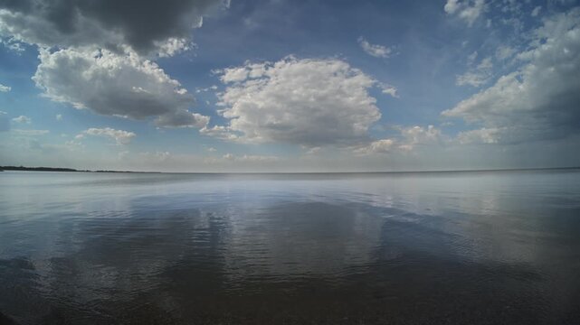 White cumulus clouds reflecting in a large calm lake with small wave distorting the clouds
