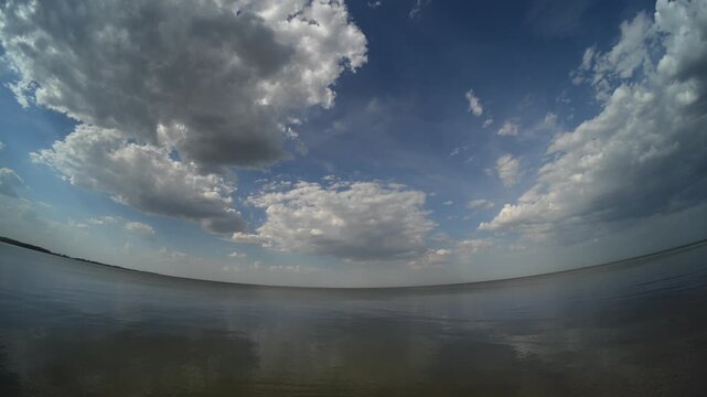 Fish-eye view of a large northern lake with cumulus clouds scatterd across a blue summer sky
