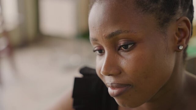 Black woman waiting for date, intimate closeup showing contemplative gaze, soft natural light, black dress shoulder detail, pearl earrings, subtle smile and nervous tear, rehearsing message, checking