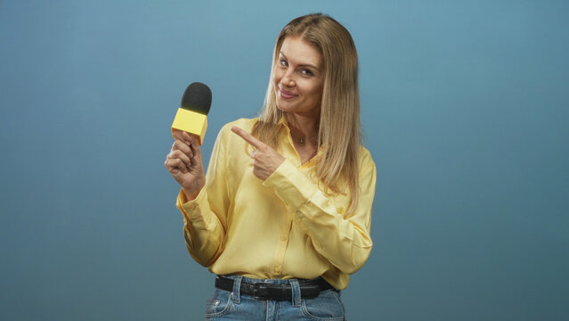 Woman reporter holding a microphone and pointing with her hand in a blue studio; confidence broadcast.