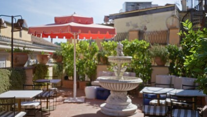 Fototapeta premium Rooftop cafe terrace scene in soft defocused bokeh with central fountain, striped chairs, umbrella and potted plants in sunny outdoor cafe; background backdrop copyspace calm.