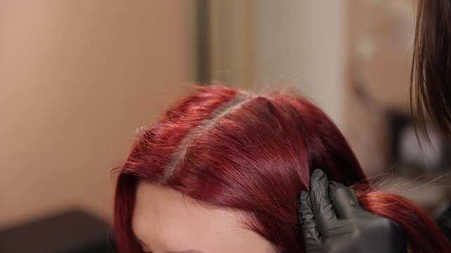 Hairdresser applying color dye to red hair roots