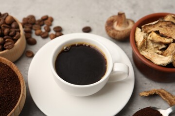 Obraz premium Cup of coffee, beans, powder and mushrooms on light grey table, closeup