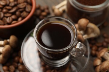 Fototapeta premium Cup of coffee, beans and mushrooms on wooden table, closeup