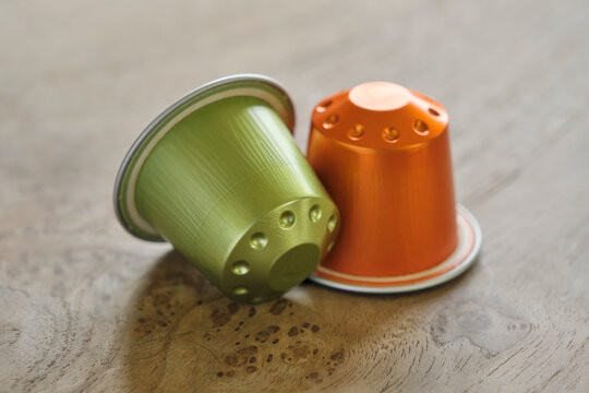 Closeup of two colorful coffee capsules in green and orange on a wooden table..