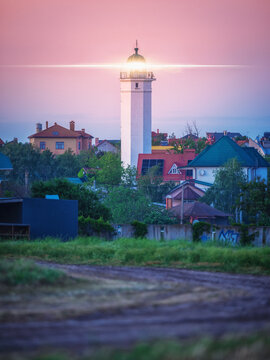 portrait view to lighthouse with signal light in village on sea shore in twilight