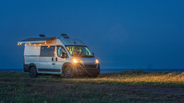 panoramic view to white camper van with romantic light in blue hour on the sea coast