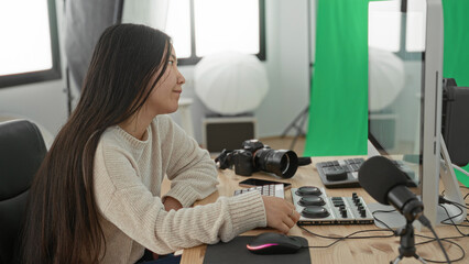 Woman at studio desk with camera and microphone, resting chin on fist while gazing at monitor and keyboard  contemplation creativity focus. © Krakenimages.com