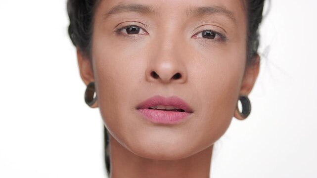 Big close-up shot of hispanic woman with bronzed skin strokes her jawline presenting revitalized skin on light background | Beauty ad concept