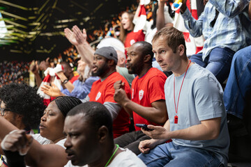 Fototapeta premium Soccer fan using betting app at the stadium during dramatic football match filled with cheering and joy. Supporter monitor live odds on gambling app, tension of sports betting and live match action.
