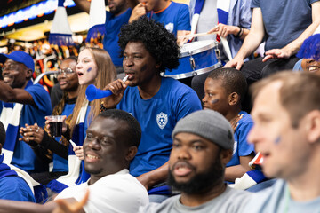 Black father with vuvuzela spending quality time with son at soccer stadium full of cheering fans. Football lifestyle, parenthood and family bonding, blue team support and childhood joy. © DC Studio