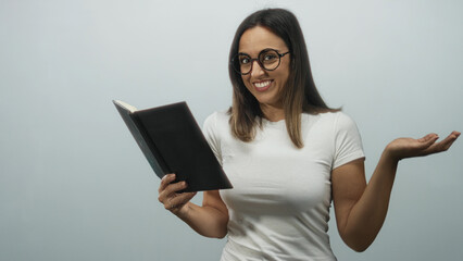 Fototapeta premium Woman reading a black hardcover book, holding it and shrugging palm up with a smile while wearing glasses in a studio; curiosity.