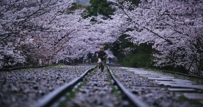 Cinematic slow motion of child with backpack running through tracks with surrounding cherry blossoms