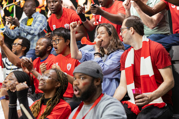 Fototapeta premium Red team football fans reacting in crowded stadium stands with red vuvuzelas, scarves and mixed emotions during soccer match. Organized soccer ultras singing and making noise for team support.