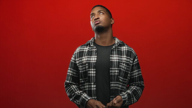 Man holds wrench in studio with visible hand and apathetic facial gesture, plaid shirt against red backdrop; quiet contemplation.