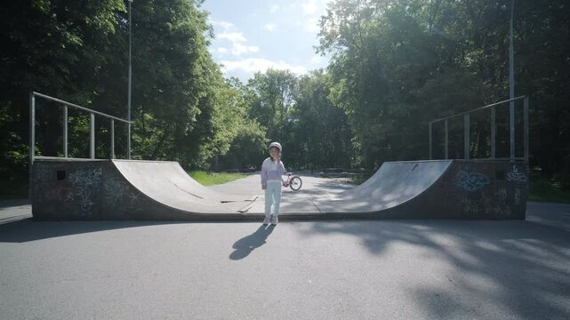 Child in a helmet posing at a public skate park in summer.