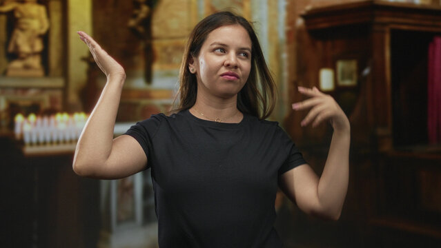 Young woman shrugging with hands raised palms up near votive candles in church building; indifference doubt.