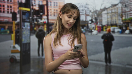 Obraz premium Woman holding smartphone and touching hair on street with navel exposed; contentment youth connection.