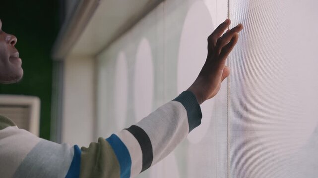Hands exploring textured blind surface. Closeup of fingers tracing concentric pattern on sheer window blind, striped sleeve visible, studio apartment backdrop, tactile curiosity and design inspection