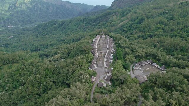 Aerial view of Bena Traditional Village with thatched roof houses nestled in a lush green valley surrounded by mountains in Kecamatan Jerebuu, Nusa Tenggara Timur, Indonesia.