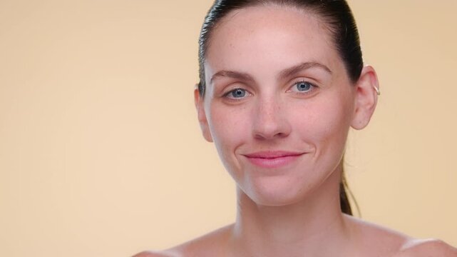 BCU shot of light-complexioned freckled Latina strokes under-eye area with fingers of both hands demonstrating elastic skin on neutral background