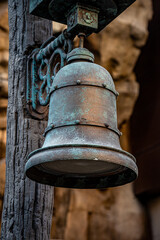 Fototapeta premium Close-up of an old, weathered bronze bell with verdigris patina on a textured wooden post