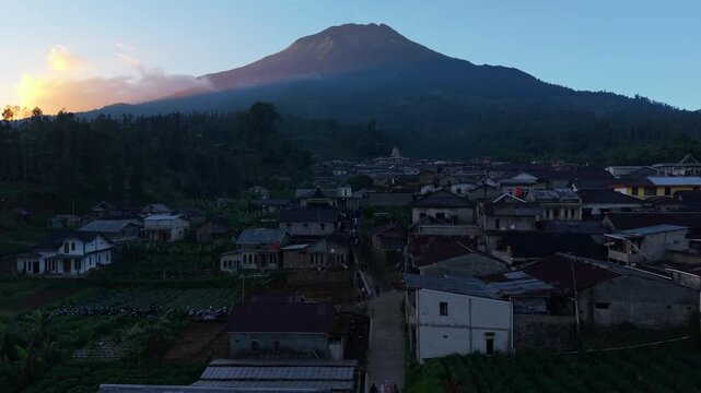 Aerial view of Garung village nestled at the foot of a majestic mountain with houses and lush greenery during golden hour Kecamatan Kalikajar, Jawa Tengah, Indonesia.