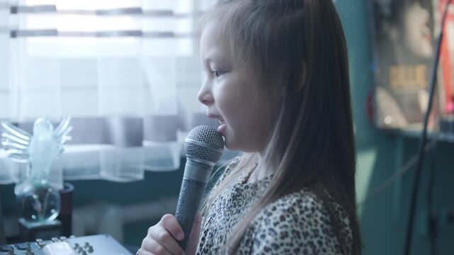 Little girl singing into a microphone during a vocal lesson with a teacher in a music studio.