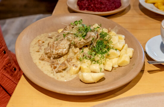 Plate of Polish kopytka potato dumplings with meat in creamy mushroom sauce, fresh dill and microgreens on wooden restaurant table, hearty European dinner close-up with beetroot side dish