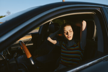 Obraz premium Woman sitting inside a car, striped shirt, thoughtful expression, hands in hair. Close-up on interior. Lifestyle portrait with casual driving mood and retro film color palette. Soft lighting adds