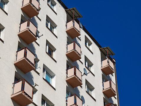 Old apartment building facade with rows of small balconies, windows and satellite dishes against clear blue sky, Eastern European block of flats renovation and real estate concept, no people