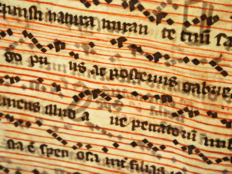 Macro close-up of antique Gregorian chant manuscript on parchment with black neume notation, red staff lines and Latin text, medieval church music sheet, weathered sacred music document, no people