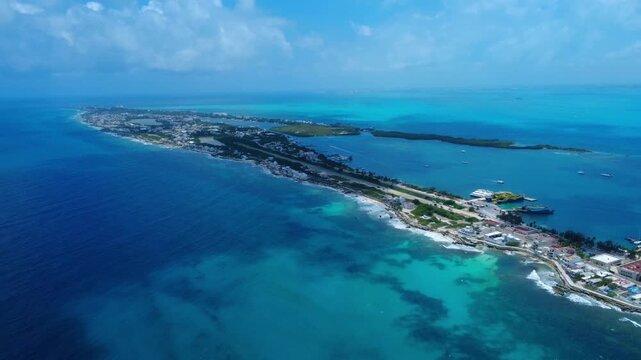 Wide aerial view of Isla Mujeres, Mexico, showcasing the entire narrow island landscape. Beautiful 4K drone shot pulling back over deep blue and turquoise Caribbean waters.