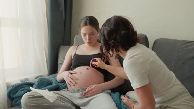 Pregnant caucasian woman receiving prenatal check from midwife using handheld monitor on belly seated on couch near window, focused clinical yet warm home visit, attentive professional assessing fetal