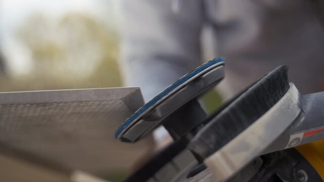 Worker is polishing edge of ceramic tile with an grinder on a workbench during a home project. Close up