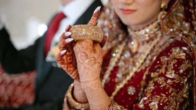 Indian bride holding traditional bridal bangles during wedding ceremony preparation. Elegant henna details, luxury jewelry, and cultural wedding attire.