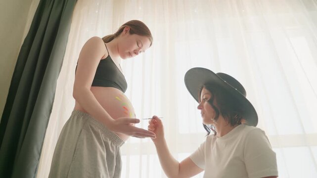 Pregnant woman belly painting in sunlit room, friend artist decorating round belly with colorful heart, soft curtains, warm glow, tender bonding moment, playful maternity celebration, gentle brush