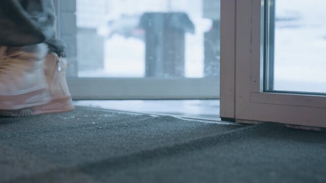 Snowy boots entering cafe doorway mat, closeup of rubber mat and glass door, soft morning light, wet footprints and cold air outside, slow step suggesting calm arrival into warm interior near brick