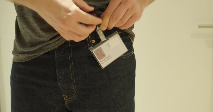 Close-up of a person attaching an employee identification badge to jeans using a clip. Concept of workplace identification, staff access, employee credentials, office security, and corporate identity.