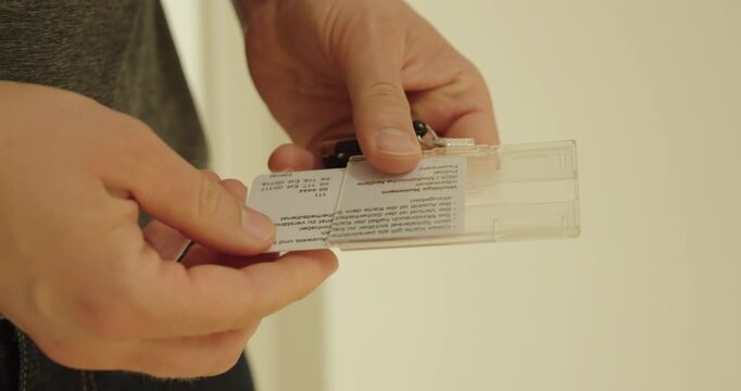Close-up of a person inserting an identification card into a transparent badge holder. Concept of employee identification, workplace access, staff credentials, office security, and corporate administr