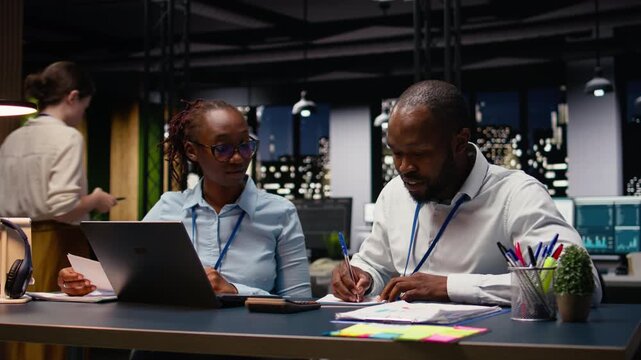 Two staff members reading emails and solving tasks together on laptop at desk, office workers analyzing data on notebook. Accounting work and interpreting statistical information.