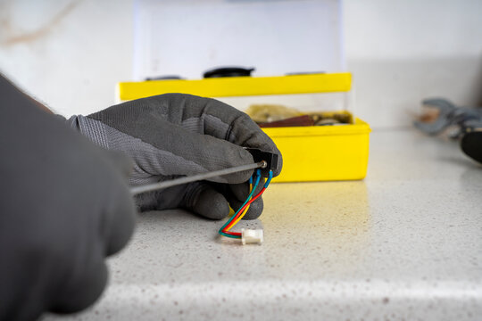 Technician using thin screwdriver to fix small screw on electric microswitch with colored wires, preparing part for gas water heater repair.