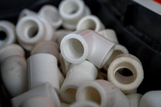 Close up of a pile of white polypropylene plastic plumbing fittings, elbows, and couplings inside a storage box compartment.