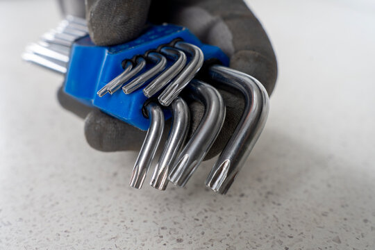 Hand in a grey protective glove holding a set of star torx key l-wrenches inside a blue plastic organizer holder on a light countertop.