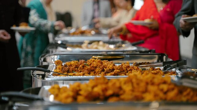 Variety of colorful spiced dished mixed at buffet event. The dish is vibrant, steaming in a festive setting, with hands using tongs