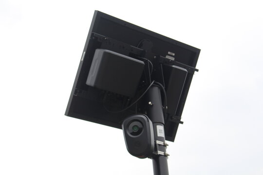 Low-angle close-up photograph of a solar-powered surveillance camera mounted on a metal pole.