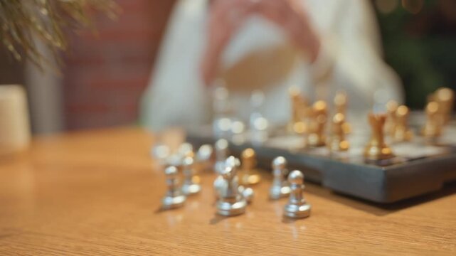 Closeup chess pieces on cafe table, silver and gold knights and pawns sitting on warm wood with shallow depth of field, white player holding piece in thoughtful pause, soft Christmas bokeh lights,