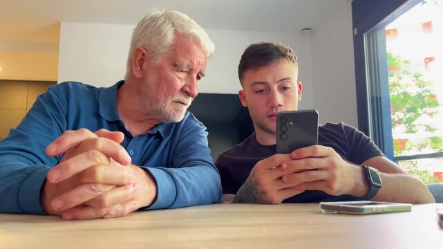 A young man teaches an older man how to use a smartphone, bridging the generational technology gap and fostering connection between them.