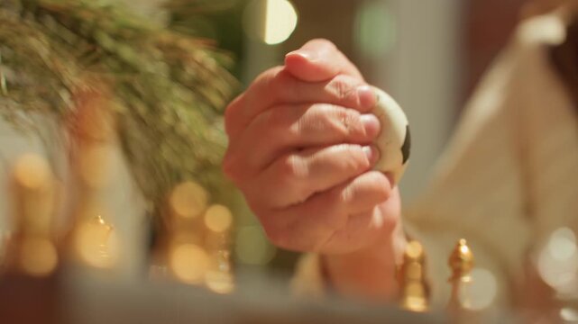 Close up hands gripping stress ball beside chess pieces on tabletop, warm cafe lights and shallow bokeh, firm clasp and subtle tremor, strategy pause before move, golden pieces and blurred background