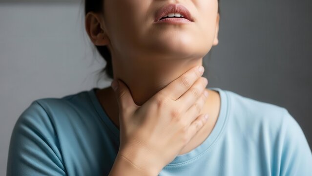 A woman experiencing a sore throat, holding her neck in discomfort.